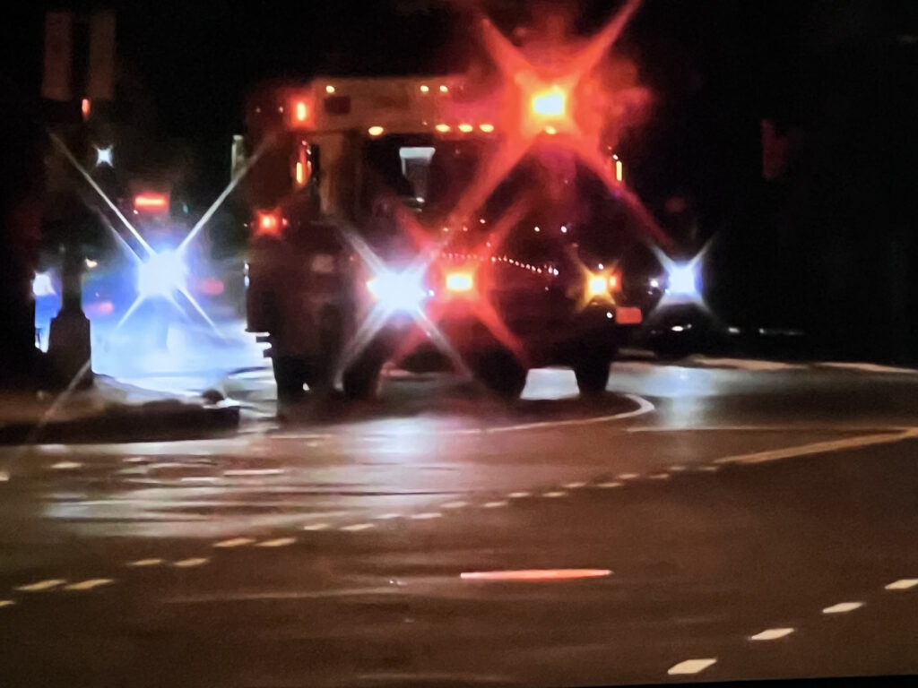 Ambulances with their lights flashing in the evening along a highway.
